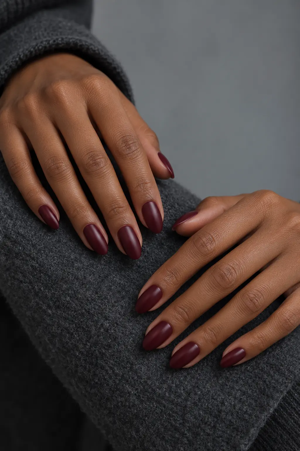 Burgundy Satin Almond nails in a satin burgundy shade perfect for late fall nails resting on a gray knit sweater