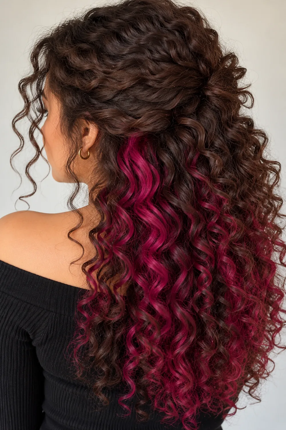 Curly hair with magenta peekaboo color showing through the curls