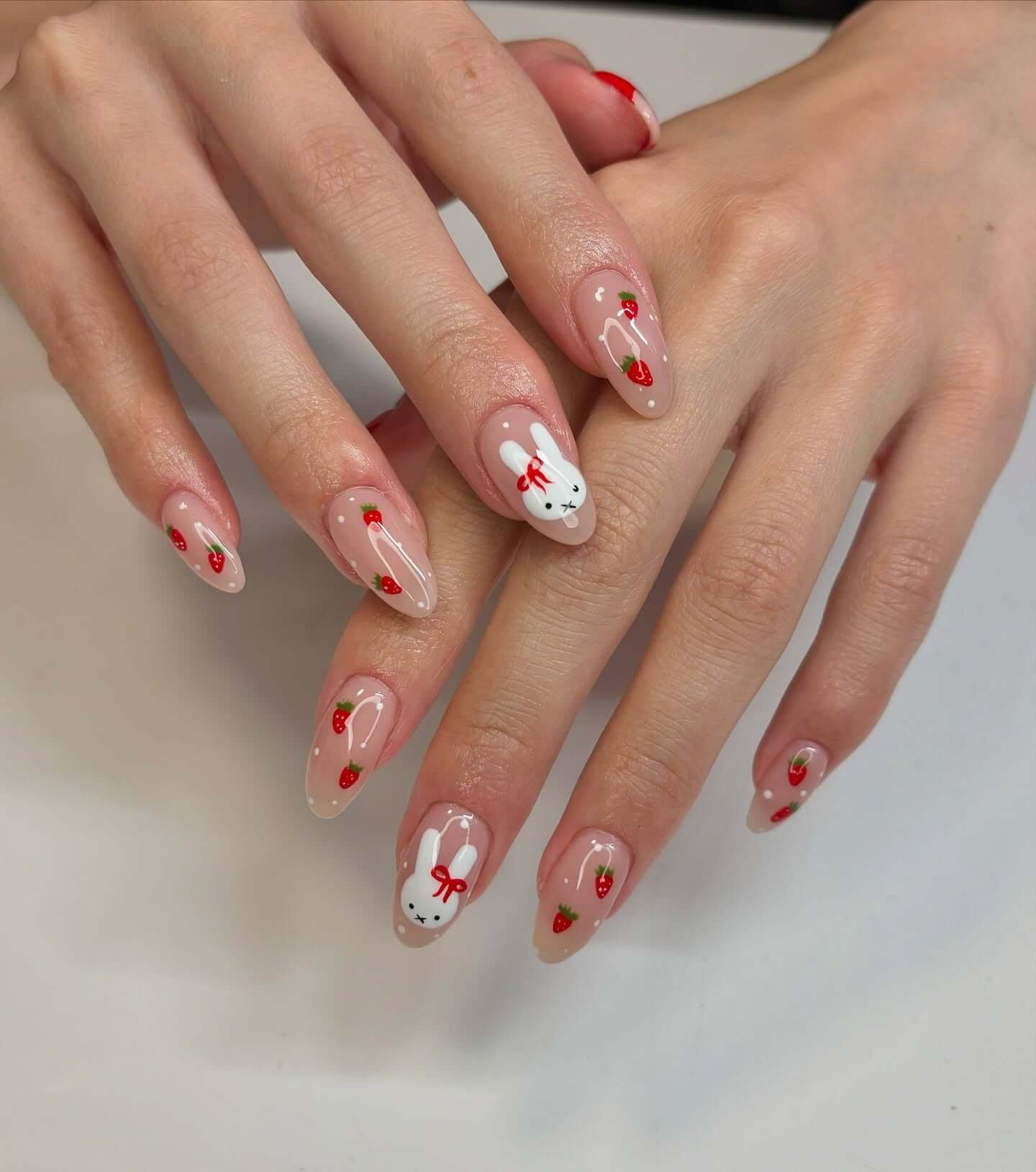 Tiny Strawberries on Sheer Nude: Medium almond sheer nude nails with tiny red strawberries and white dots