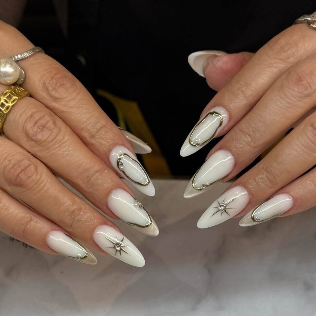 Milky white almond nails with a thin gold outline and tiny gems